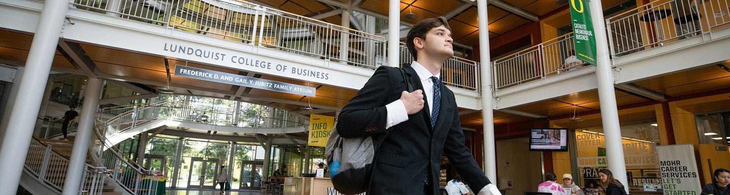 One student wearing a suit and carrying a backpack walking through the Lillis Complex atrium